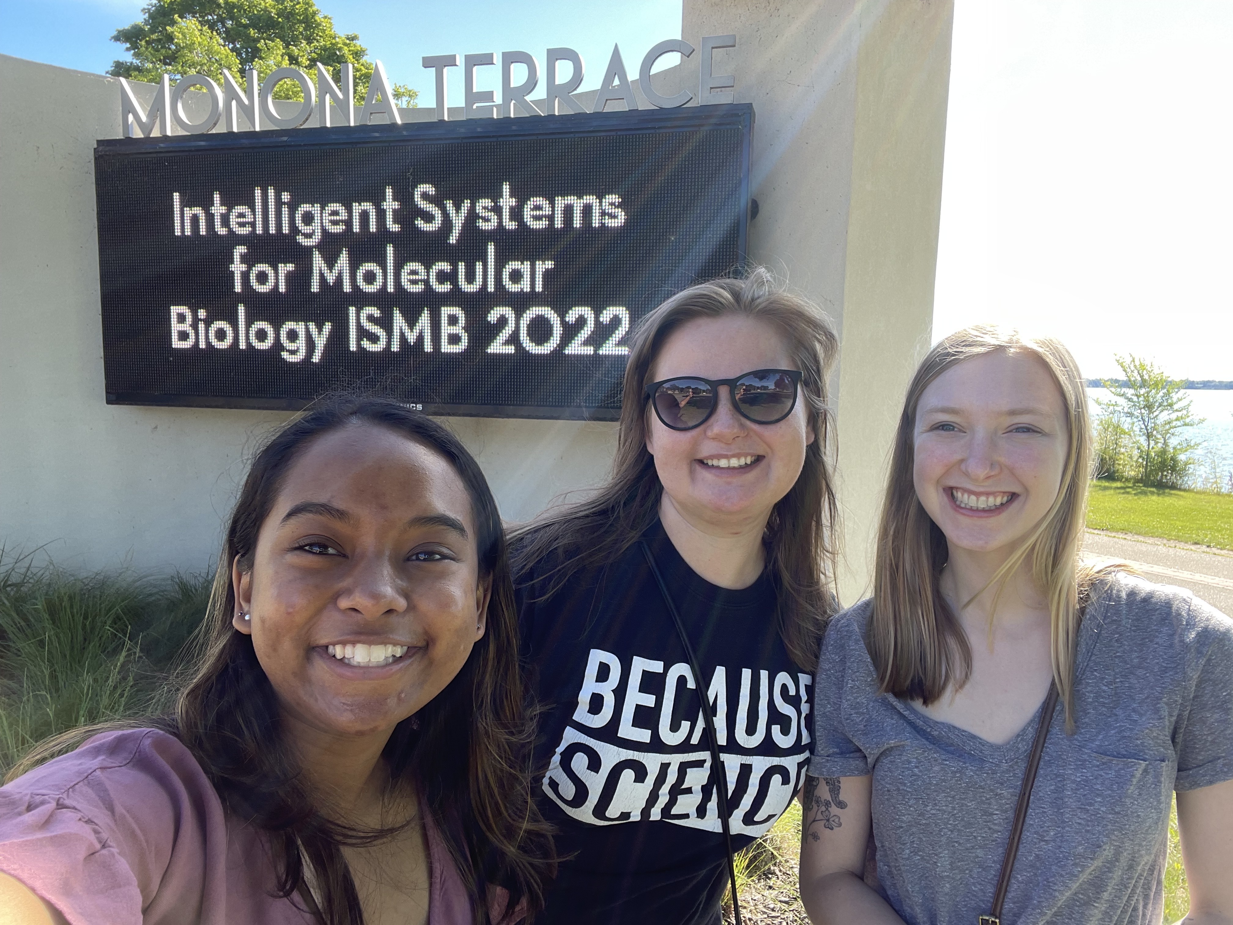 A picture of Anisha, Jen, and Emma in front of a sign for the conference
